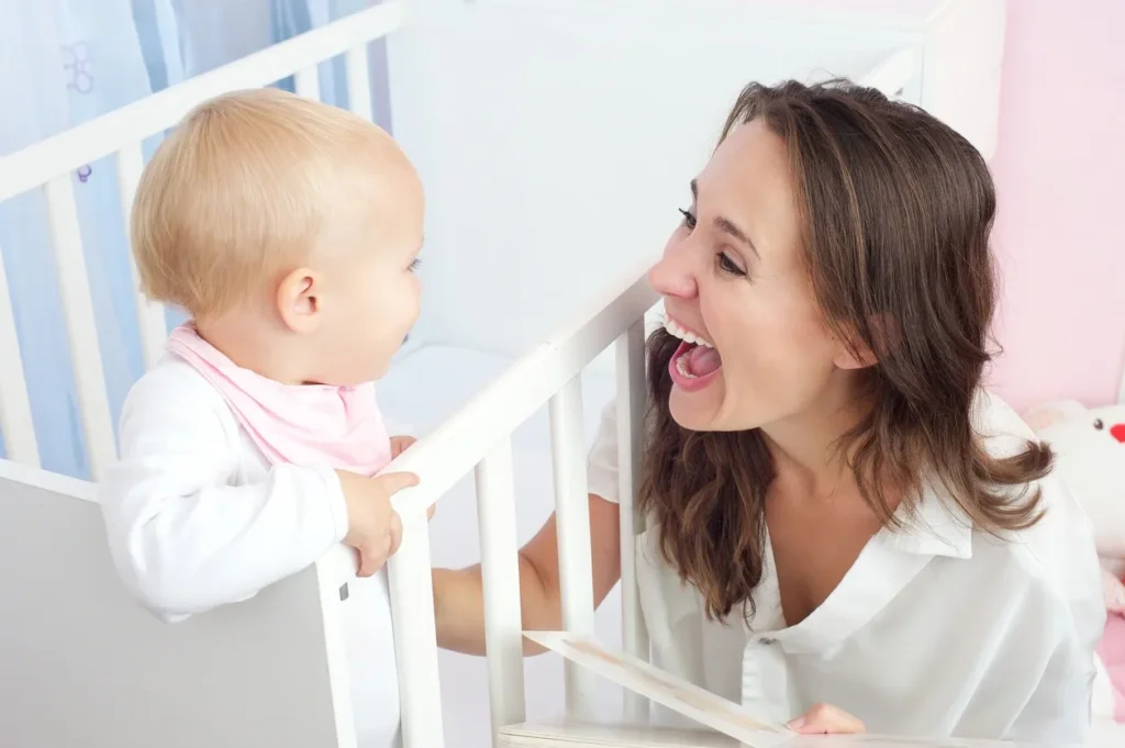 A mother joyfully interacts with her baby in a crib.