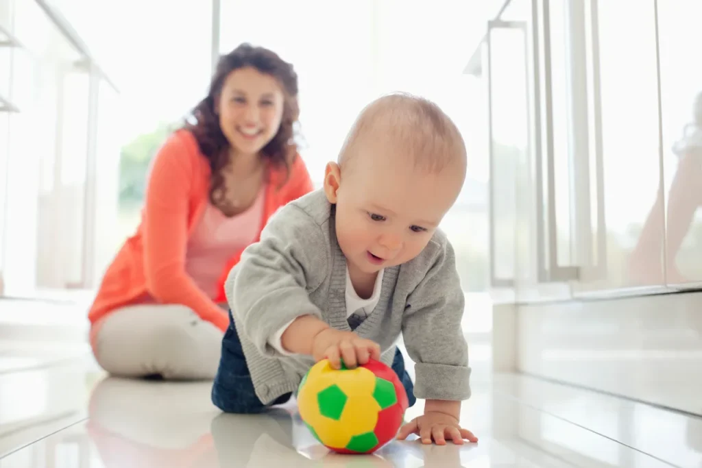A baby playing with a colorful ball while mom watches happily.